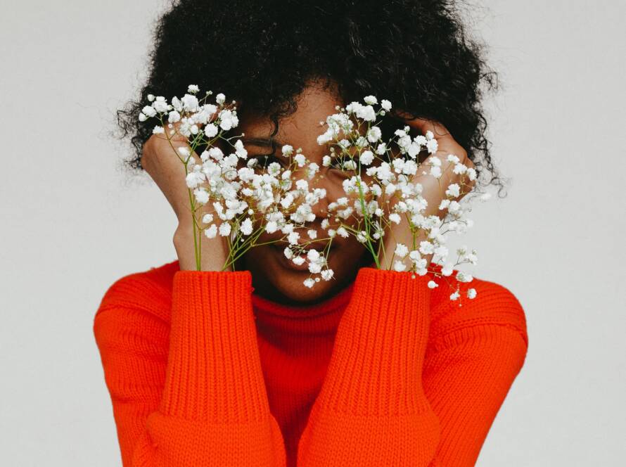 A person in an orange sweater holds white flowers in front of their face, creating a serene image.