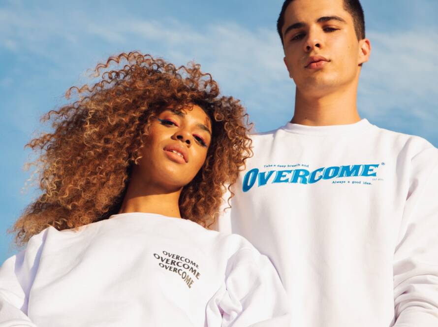 Two people wearing white sweatshirts with the word "OVERCOME" in front of a blue sky.