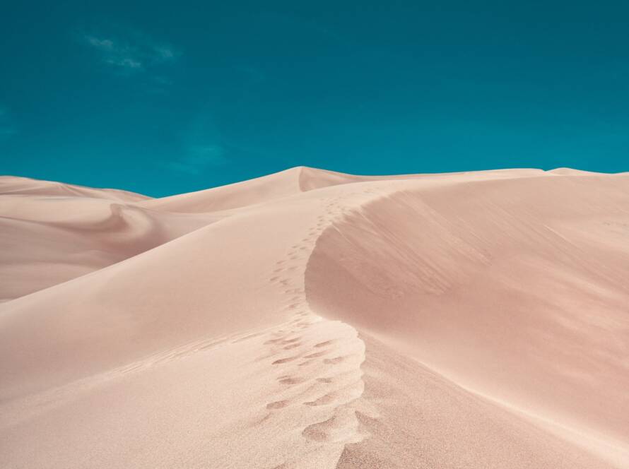 Footprints in the sand on a desert dune with a clear blue sky above