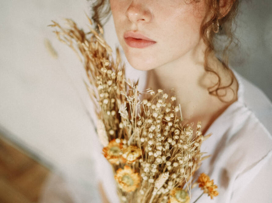 A beautiful young woman with curly hair and blue eyes holding a bouquet of dried flowers.