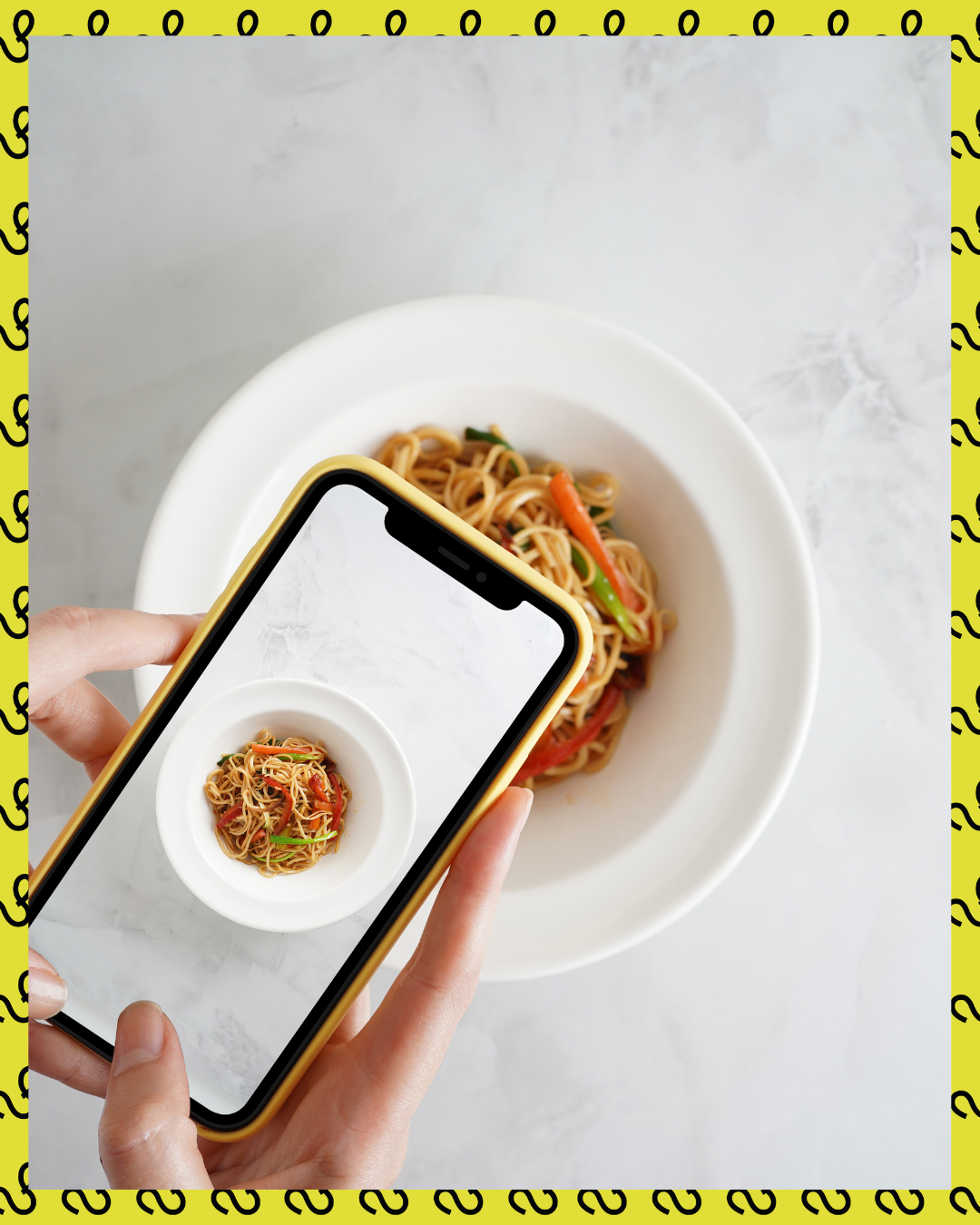 A person taking a photo of noodles on their phone, which is over a big bowl of noodles.