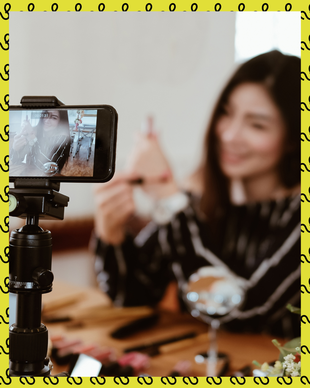 A woman filming a makeup tutorial on her phone, with beauty products on the table.